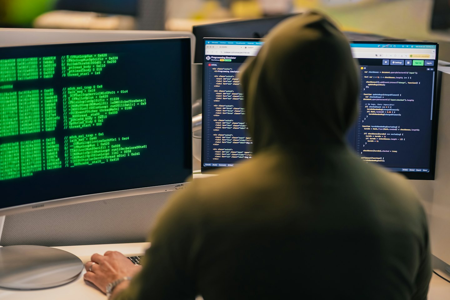 Ein Programmierer im Hoodie arbeitet an zwei Monitoren mit Code.